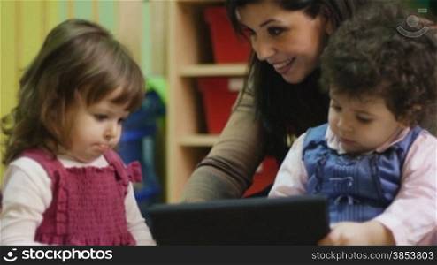 Teacher and little girls playing with laptop computer in kindergarten