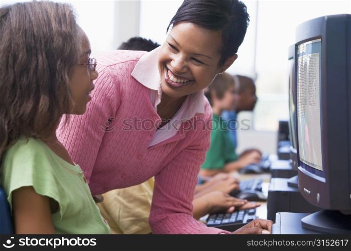 Teacher helping a student at computer terminal with students in background (selective focus/high key)