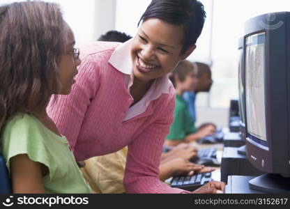 Teacher helping a student at computer terminal with students in background (selective focus/high key)