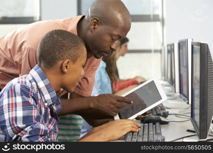 Teacher Helping Boy To Use Digital Tablet In Computer Class