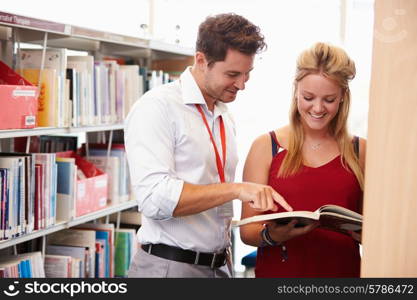 Teacher Helping College Student With Studies In Library