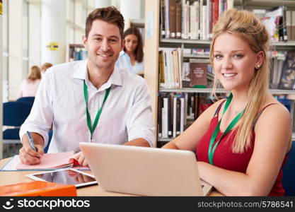 Teacher Helping College Student With Studies In Library