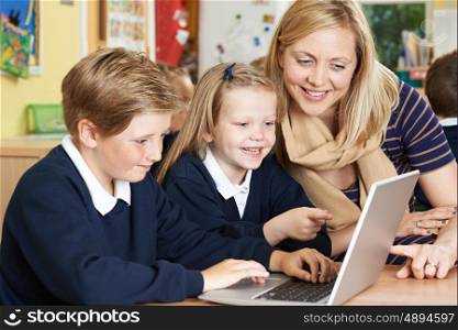 Teacher Helping Elementary School Pupils In Computer Class
