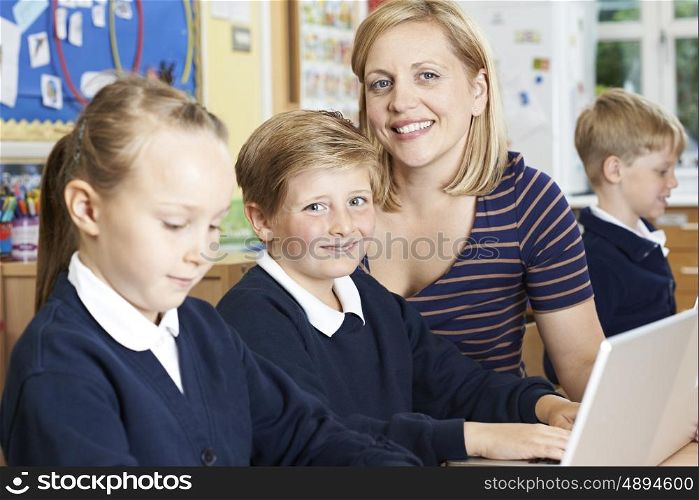 Teacher Helping Elementary School Pupils In Computer Class