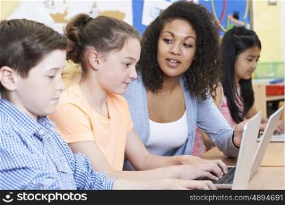 Teacher Helping Female Elementary Pupil In Computer Class