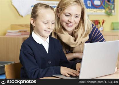 Teacher Helping Female Elementary School Pupil In Computer Class