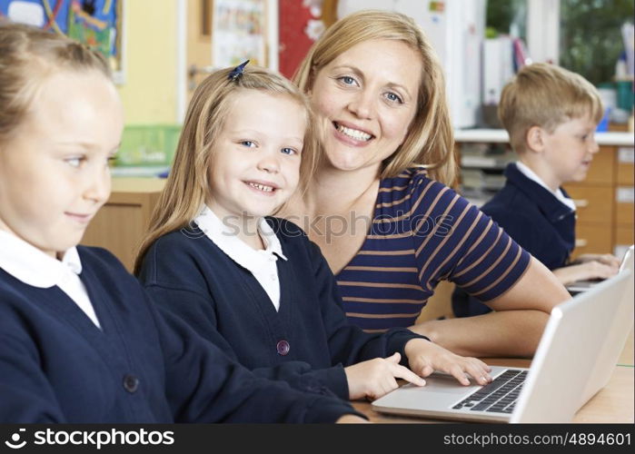 Teacher Helping Female Elementary School Pupils In Computer Class