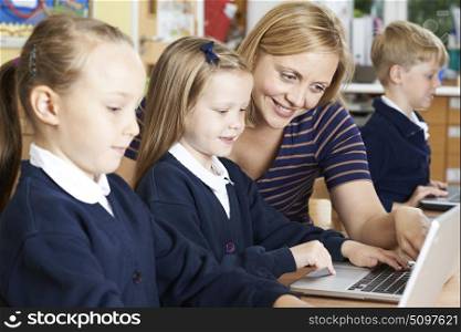 Teacher Helping Female Elementary School Pupils In Computer Class