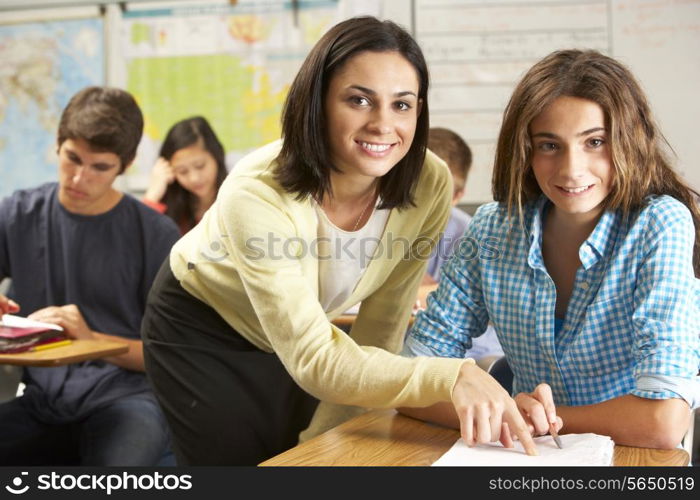 Teacher Helping Female Pupil Studying At Desk In Classroom