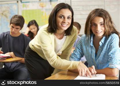 Teacher Helping Female Pupil Studying At Desk In Classroom