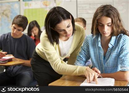 Teacher Helping Female Pupil Studying At Desk In Classroom