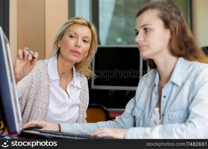 teacher helping female student using computer in classroom