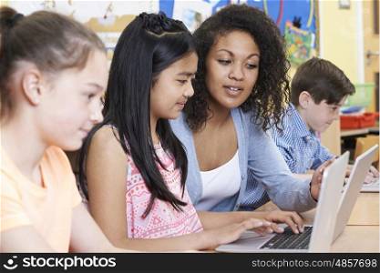 Teacher Helping Group Of Elementary School Children In Computer Class