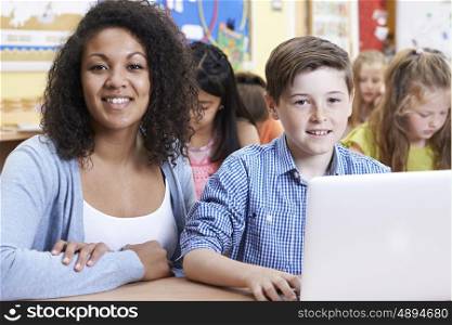 Teacher Helping Male Elementary Pupil In Computer Class