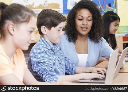 Teacher Helping Male Elementary Pupil In Computer Class