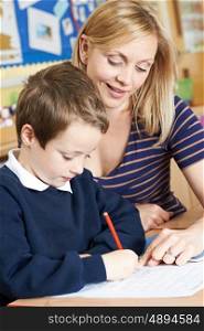 Teacher Helping Male Elementary Pupil Working At Desk