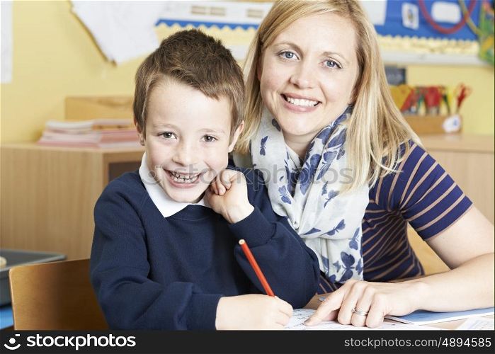 Teacher Helping Male Elementary Pupil Working At Desk