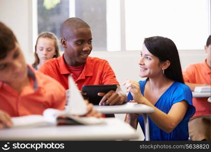 Teacher Helping Male High School Student In Classroom