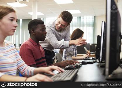 Teacher Helping Male High School Student Working In Computer Class