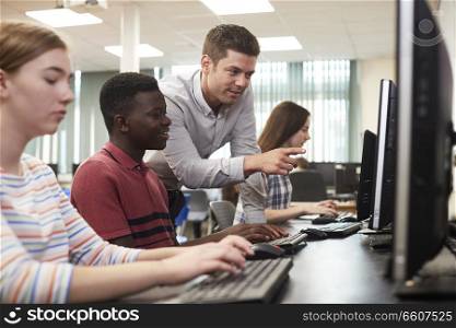 Teacher Helping Male High School Student Working In Computer Class