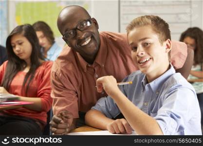 Teacher Helping Male Pupil Studying At Desk In Classroom