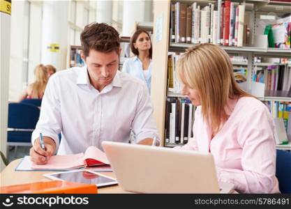 Teacher Helping Mature Student With Studies In Library