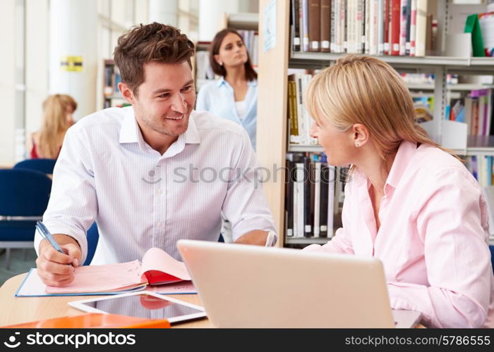 Teacher Helping Mature Student With Studies In Library