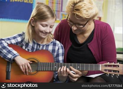 Teacher Helping Pupil To Play Guitar In Music Lesson