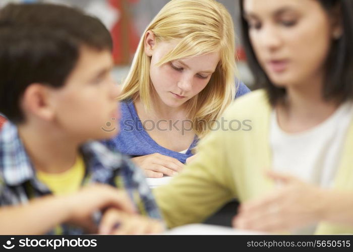 Teacher Helping Pupils Studying At Desks In Classroom