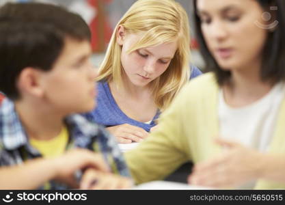 Teacher Helping Pupils Studying At Desks In Classroom