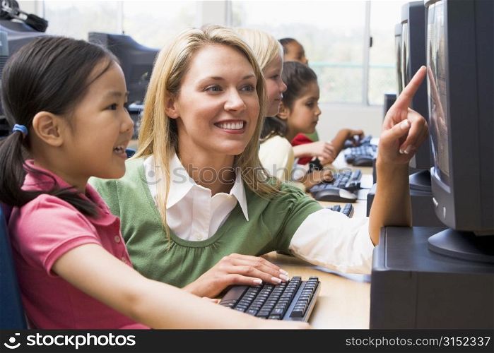 Teacher helping student at computer terminal with students in background (depth of field/high key)