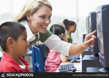 Teacher helping student at computer terminal with students in background (selective focus/high key)