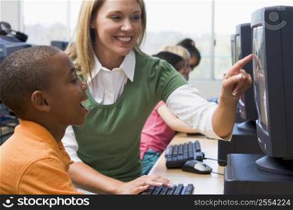 Teacher helping student at computer terminal with students in background (selective focus/high key)
