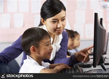 Teacher Helping Student During Computer Class In Chinese School Classroom