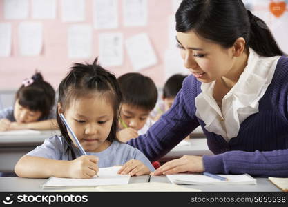 Teacher Helping Student Working At Desk In Chinese School Classroom