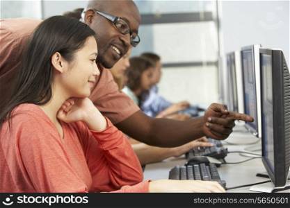 Teacher Helping Students Working At Computers In Classroom