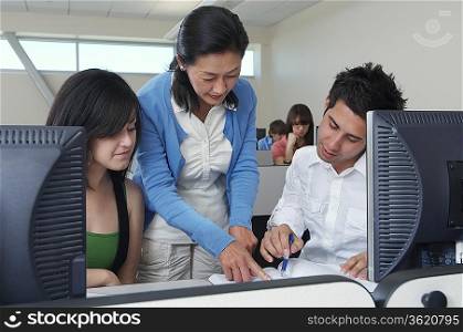 Teacher helping two students working in computer classroom