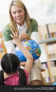 Teacher in class showing a globe with student volunteering in foreground (selective focus)