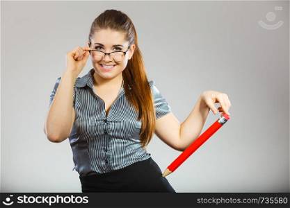 Teacher looking elegant woman wearing dark tight skirt, shirt and eyeglasses holding big oversized pencil. Teacher looking elegant woman holding big pencil