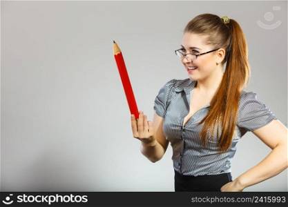 Teacher looking elegant woman wearing grey shirt and eyeglasses holding big oversized pencil. Teacher looking elegant woman holding big pencil