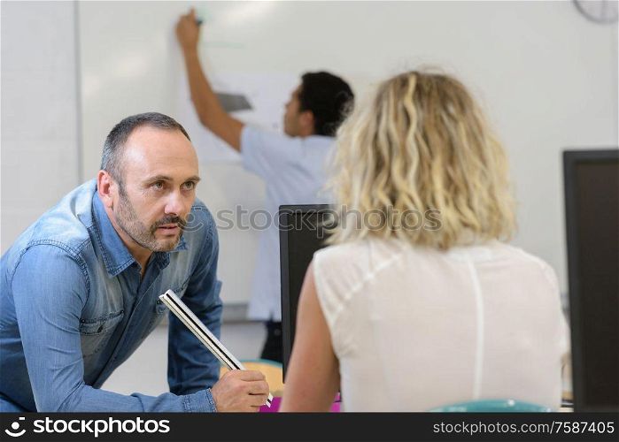 teacher questions female student while boy writes on whiteboard
