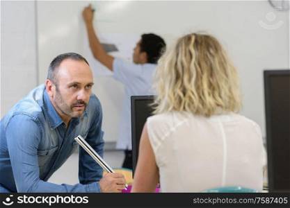 teacher questions female student while boy writes on whiteboard