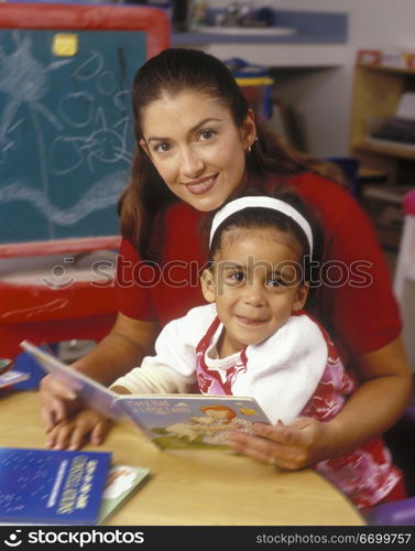 Teacher Reading Book With Little Girl In Classroom