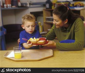 Teacher Serving Child Lunch In Preschool Classroom