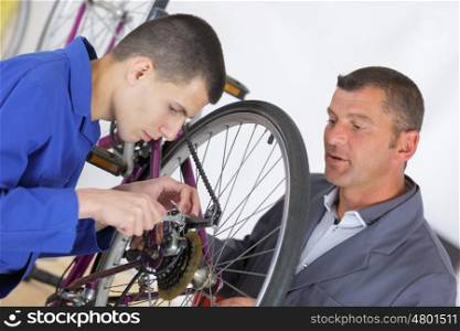 teacher showing aprentice how to fix a bike
