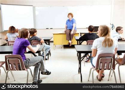 Teacher sitting on her desk, teaching a class of teenage students.