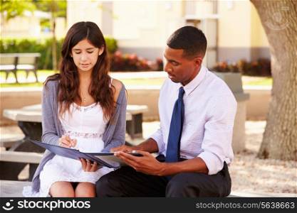 Teacher Sitting Outdoors Helping Female Student With Work