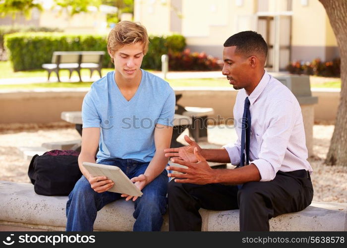 Teacher Sitting Outdoors Helping Male Student With Work