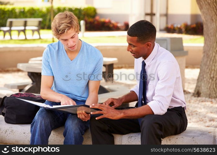 Teacher Sitting Outdoors Helping Male Student With Work