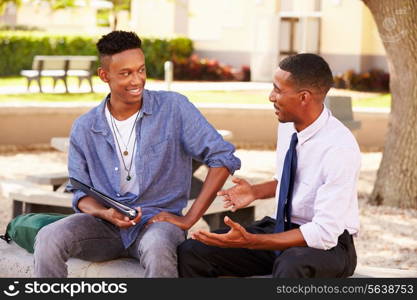 Teacher Sitting Outdoors Helping Male Student With Work